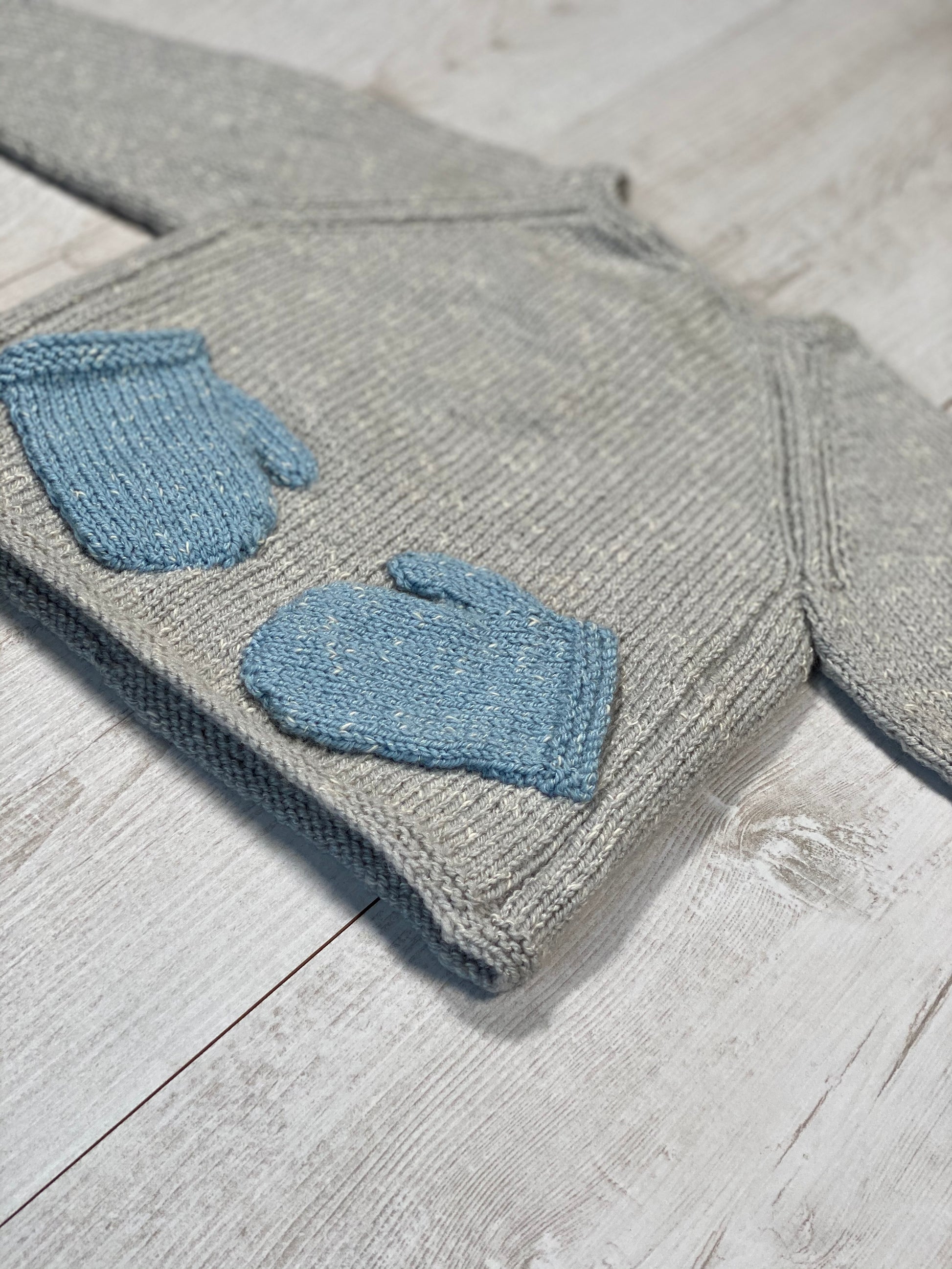 Gray knitted jumper with blue mittens on a wooden surface