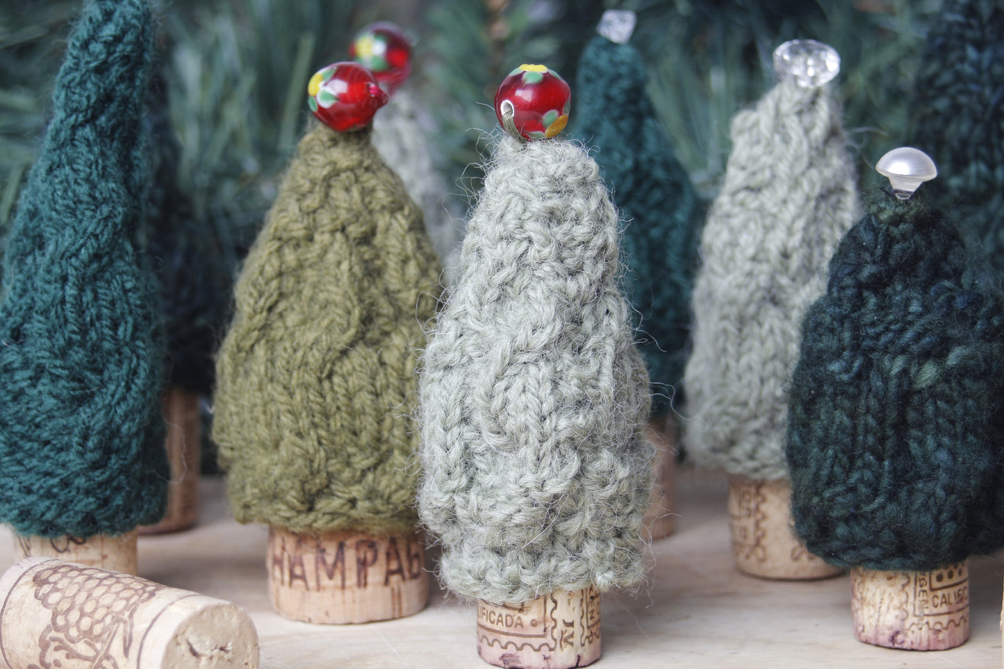 Knitted trees with colorful beads on cork bases against a blurred green background