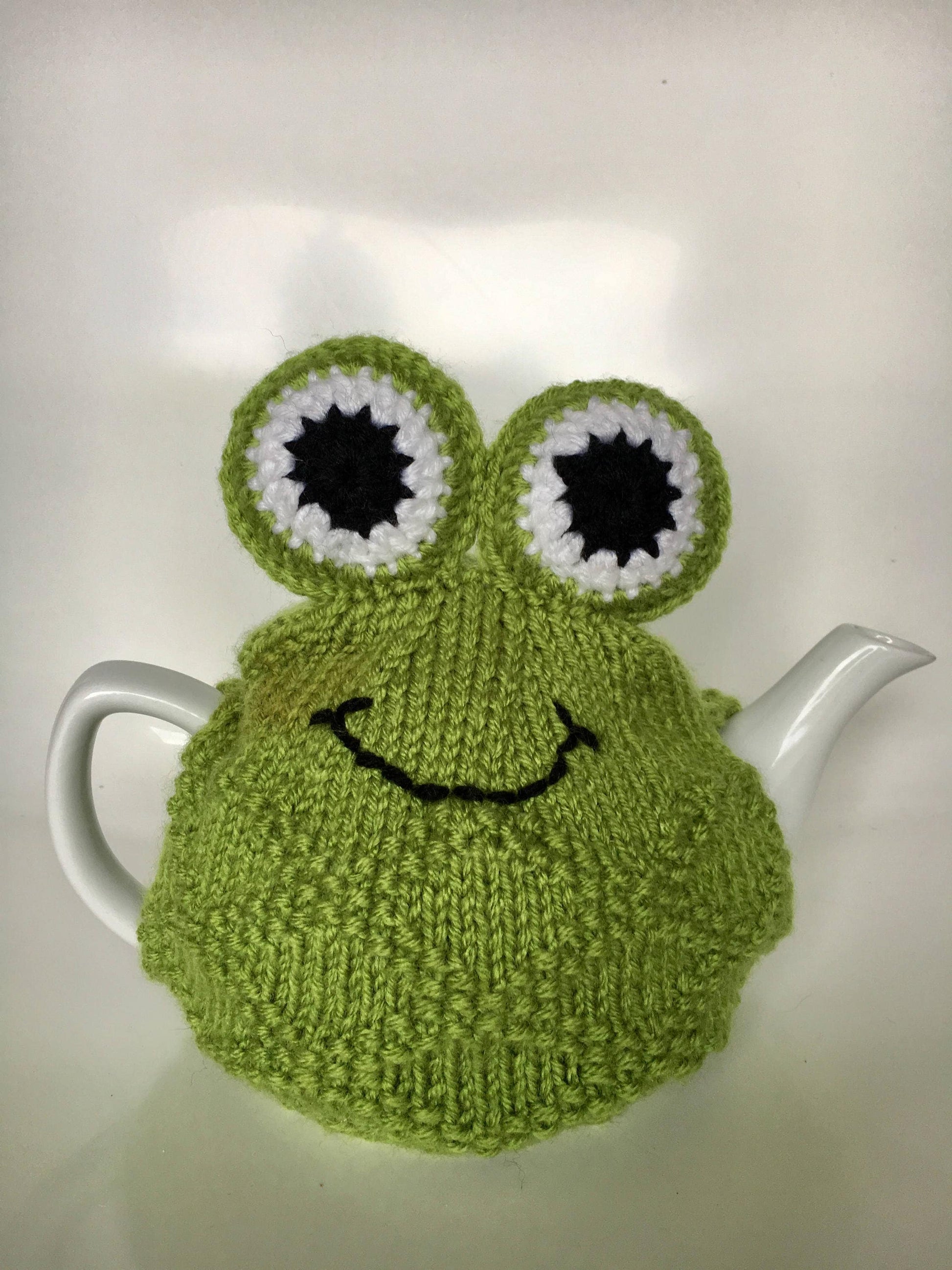 Green frog hand knitted tea cosie with large padded eyes.