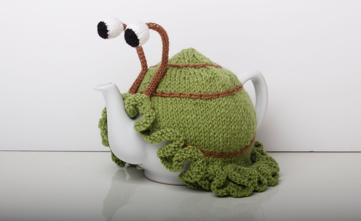 Knitted green snail tea cosy with frilly bottom. Washable fits 6 cup and 2 cup pots.