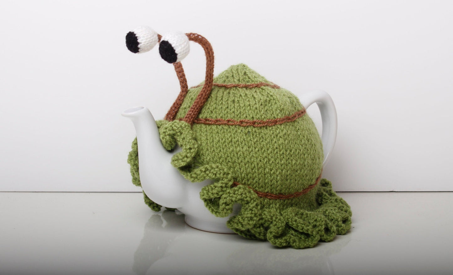 Knitted green snail tea cosy with frilly bottom. Washable fits 6 cup and 2 cup pots.