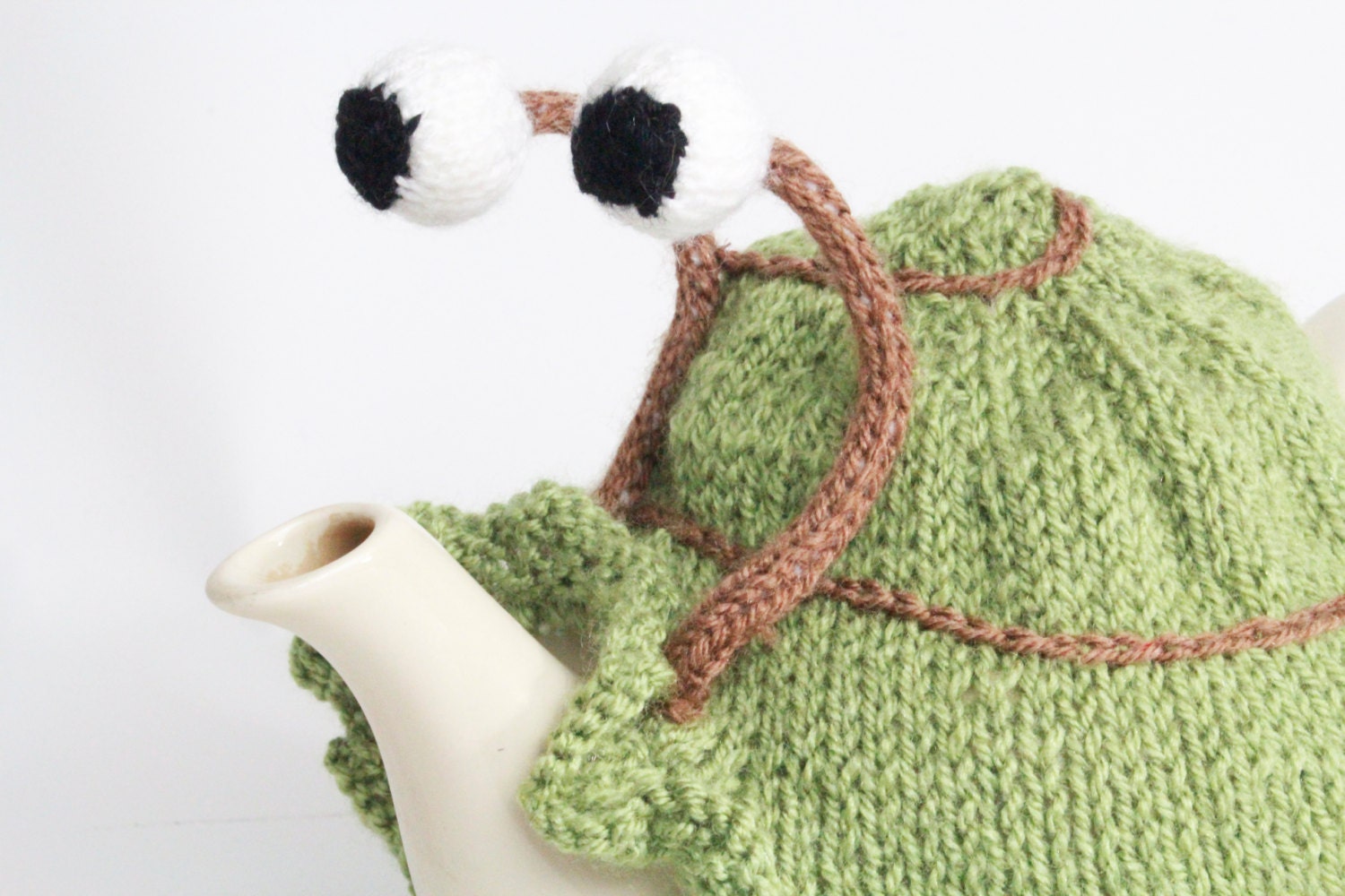 Knitted green snail tea cosy with frilly bottom. Washable fits 6 cup and 2 cup pots.